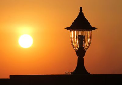 Low angle view of illuminated lamp against orange sky
