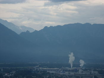 Smoke emitting from factory against mountains