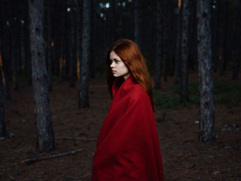 Woman standing by tree trunk in forest