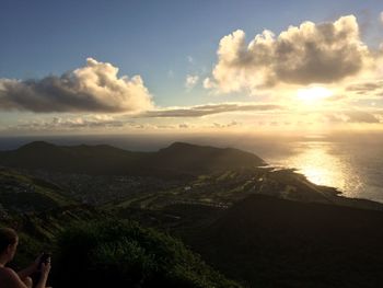 Woman using phone by mountains at coastline against sky during sunset