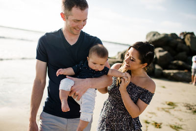 Mid 30's parents holding son walking at beach