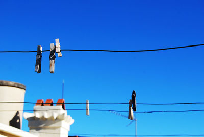 Low angle view of clothespins on ropes against clear blue sky