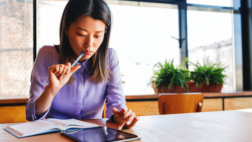 Woman holding book while sitting on table