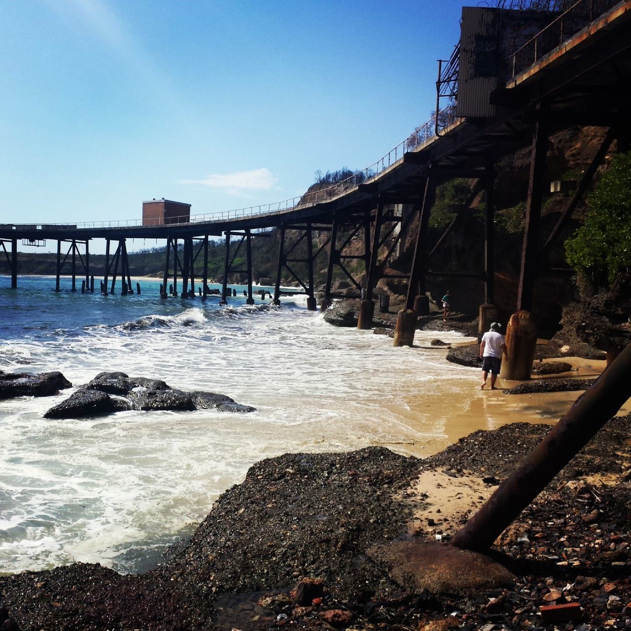 water, sea, built structure, beach, architecture, shore, wave, lifestyles, men, leisure activity, sky, surf, incidental people, rock - object, nature, bridge - man made structure, motion, clear sky