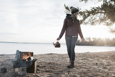 Woman walking with kettle to a campfire on a beach in sweden