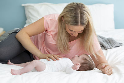 Smiling mother looking at newborn girl on bed at home