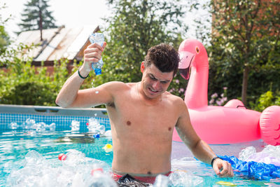 Full length of shirtless man drinking water in swimming pool