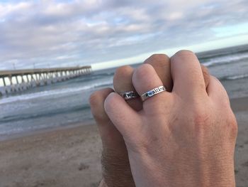 Close-up of couple wearing rings at beach against sky