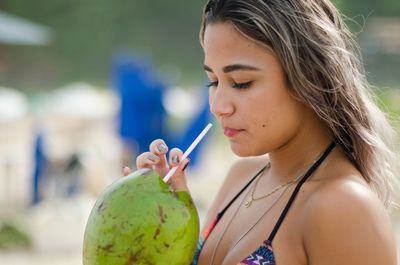 Close-up of young woman drinking coconut water at beach