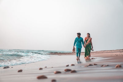 Rear view of people at beach against clear sky