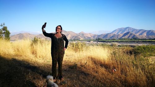 Full length of woman taking selfie while standing on field against mountains