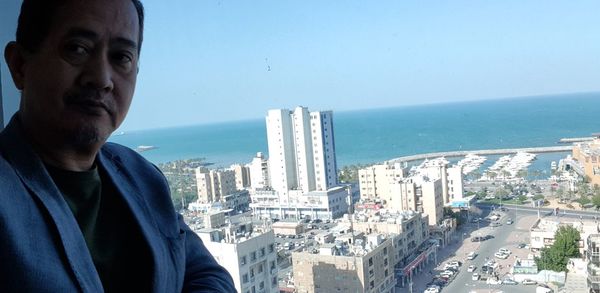 Portrait of man by sea against buildings in city