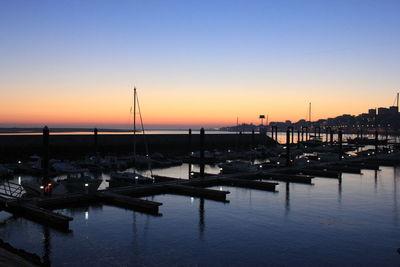 Boats moored in harbor at sunset