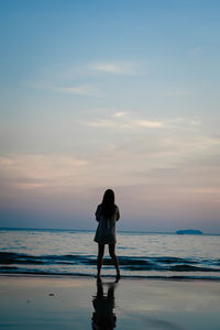 Woman standing on beach against sky during sunset