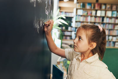 Little girl writing on blackboard. smart student put solve on chalkboard. back to school