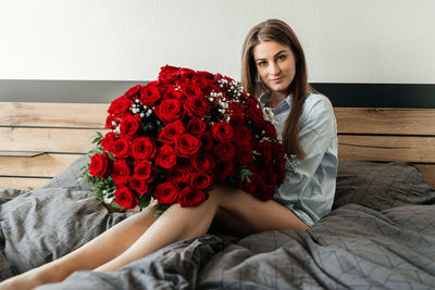 A beautiful girl is sitting on a bed in the bedroom with a huge bouquet of scarlet roses. flower 