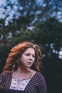 Close-up of young woman looking away against trees