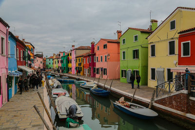 Boats moored in canal amidst buildings in city against sky