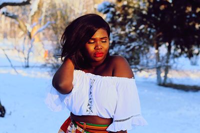 Young woman standing on snowy field against trees