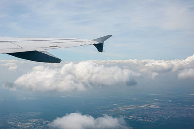 View from airborne airplane window at cloudy sky and land with fields from high altitude.