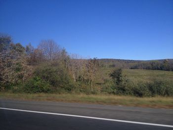 Road amidst field against clear blue sky