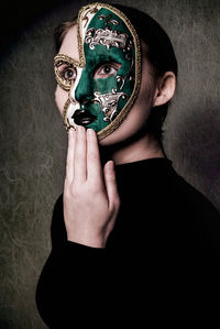 Portrait of young woman holding mask against black background