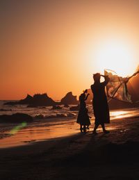 Silhouette people standing on beach against sky during sunset