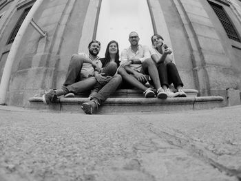 Low angle portrait of friends sitting on steps against museo nacional centro de arte rein