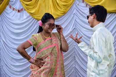 Young couple wearing sunglasses while standing against curtain