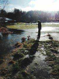 Rear view of man standing by lake against sky