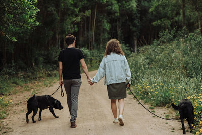 Rear view of a couple walking dogs on a leash down a forest footpath