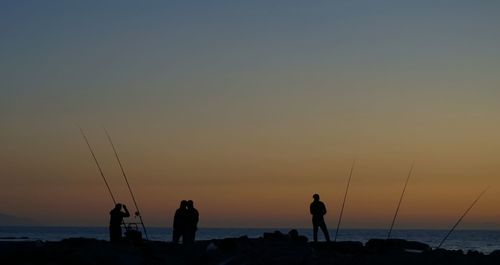 Silhouette people at beach against sky during sunset