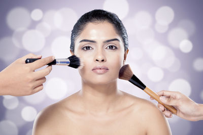 Cropped hands of people applying make-up on woman face against colored background