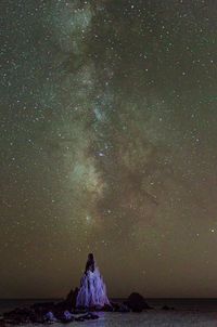 Rear view of man sitting on rock at night