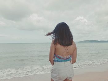 Rear view of woman standing at beach against sky