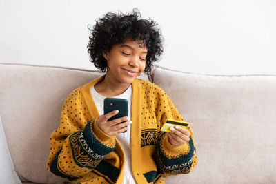 Portrait of young woman using mobile phone while sitting on sofa at home