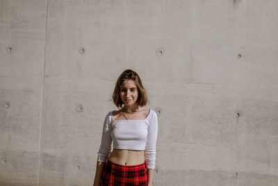 Portrait of smiling young woman standing against wall