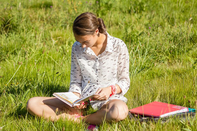 Full length of woman reading book while sitting on field