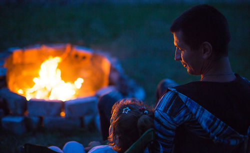 Rear view of father with daughter sitting by campfire