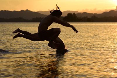 Silhouette man jumping in sea against sky during sunset