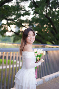 Portrait of young woman standing against trees
