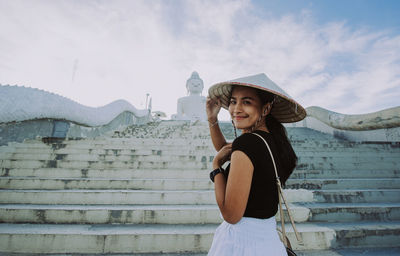 Portrait of smiling young woman standing against sky