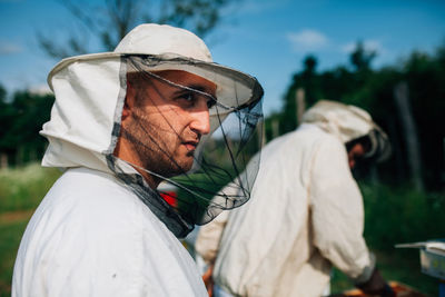 Side view of beekeepers standing by colleague on land