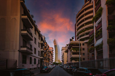 Cars on road amidst buildings against sky during sunset