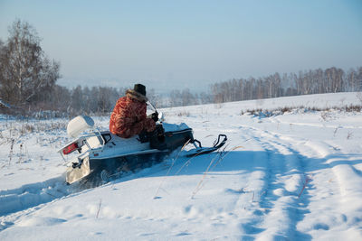 Rear view of person tobogganing on snow covered field against sky