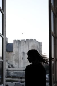 Silhouette of woman standing by window against clear sky