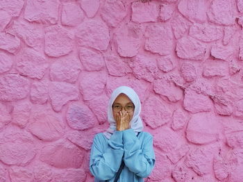 Portrait of woman standing against pink wall