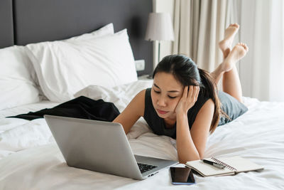 Stressed businesswoman working on laptop computer in bed at hotel.
