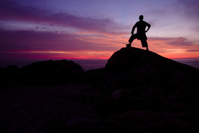 Silhouette man standing on rock against sky during sunset