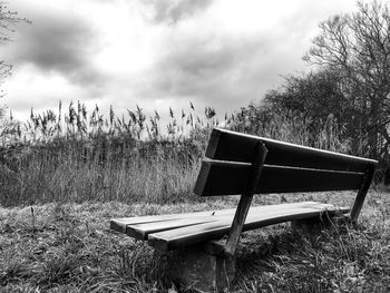Empty bench on field against sky